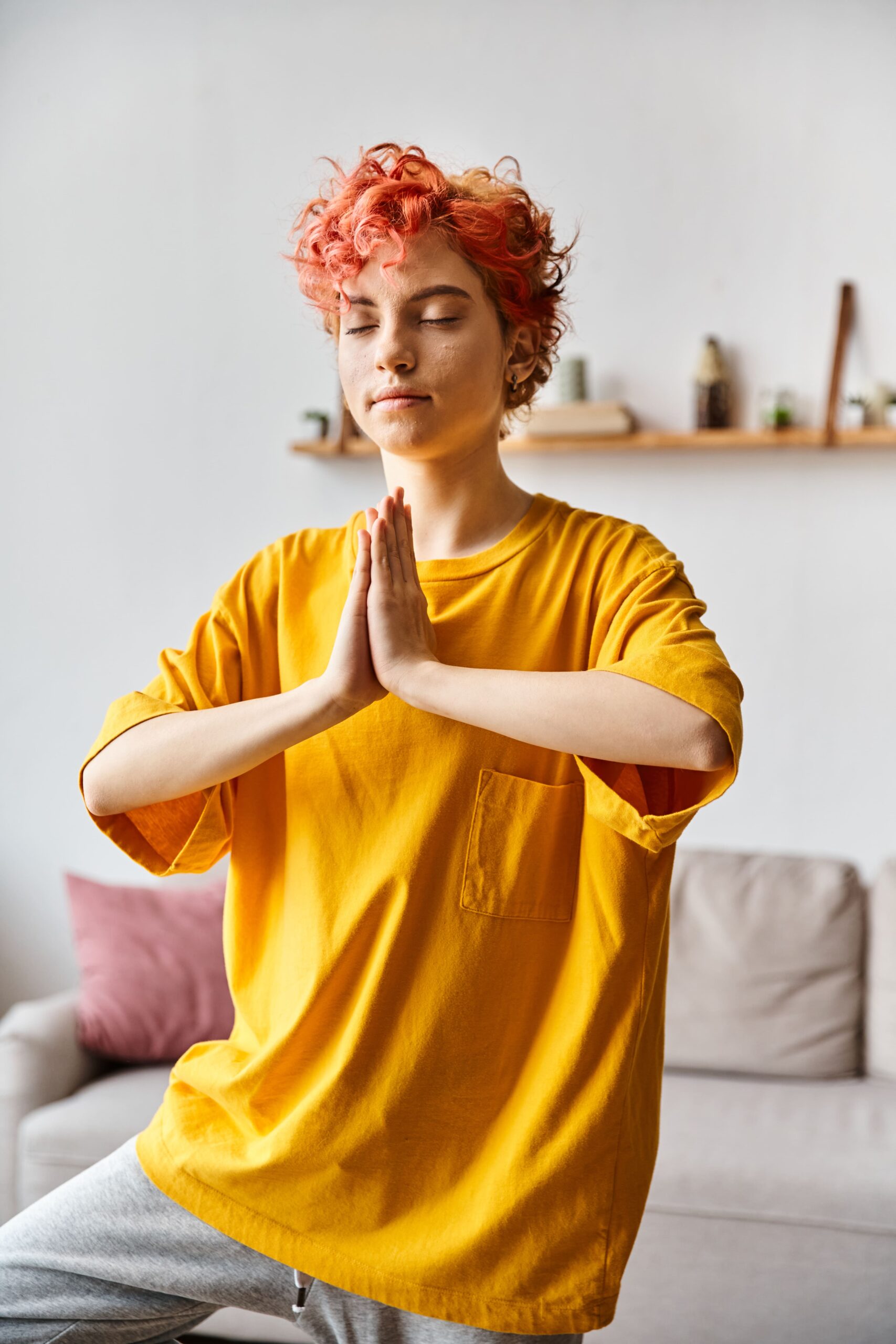 attractive-red-haired-queer-person-vivid-outfit-meditating-with-closed-eyes-while-home